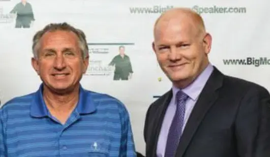 Two men smiling in front of banner.