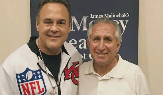Two men smiling in front of sign.