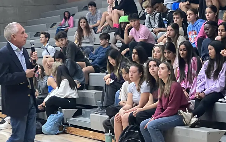 Speaker addressing seated students in gymnasium.