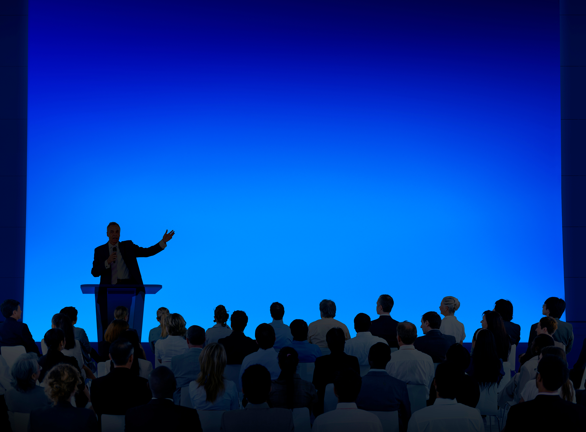 Speaker addressing audience in blue-lit room.